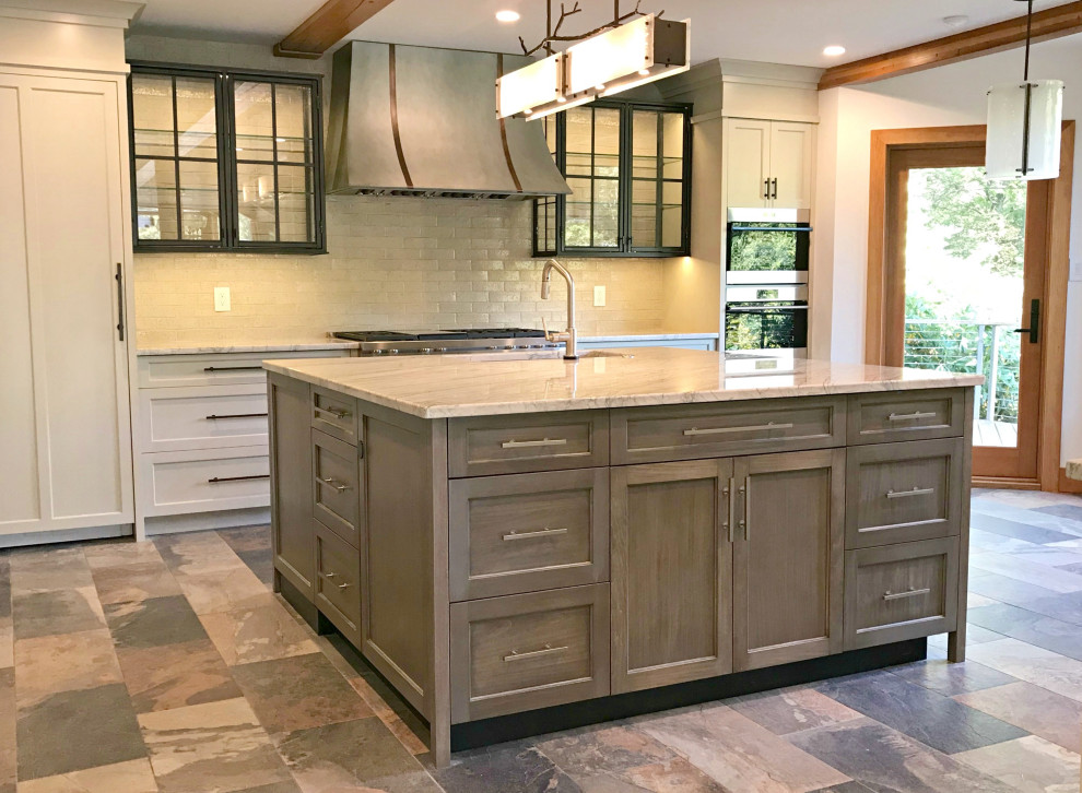 Photo of a large industrial u-shaped eat-in kitchen in Philadelphia with a farmhouse sink, flat-panel cabinets, grey cabinets, granite benchtops, beige splashback, porcelain splashback, stainless steel appliances, slate floors, with island, grey floor and white benchtop.