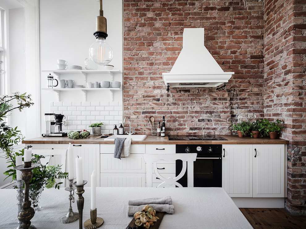 Photo of a mid-sized scandinavian single-wall eat-in kitchen in Gothenburg with white cabinets, wood benchtops, no island, a drop-in sink, white splashback, subway tile splashback, black appliances, medium hardwood floors, brown floor, beige benchtop and flat-panel cabinets.