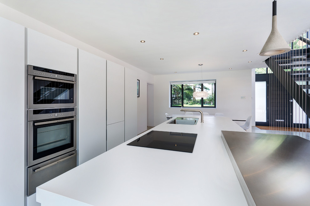Photo of a mid-sized contemporary galley eat-in kitchen in Wiltshire with an integrated sink, flat-panel cabinets, white cabinets, laminate benchtops, stainless steel appliances and with island.