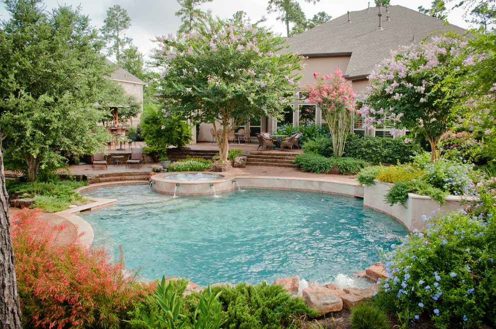 This is an example of a large traditional backyard round pool in Houston with a hot tub and natural stone pavers.