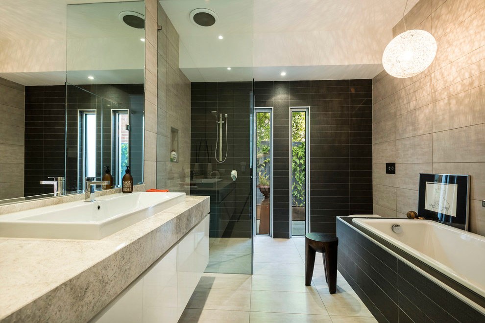 Contemporary bathroom in Melbourne with flat-panel cabinets, white cabinets, a drop-in tub, a curbless shower, black tile and a trough sink.