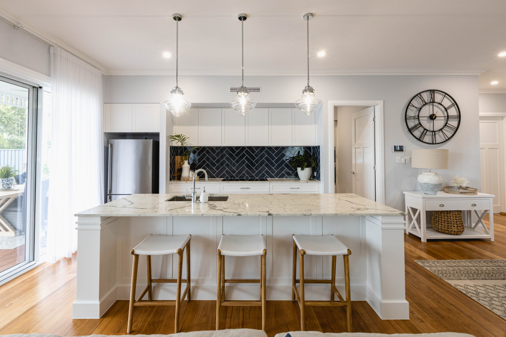 Photo of a transitional galley kitchen in Brisbane with a double-bowl sink, shaker cabinets, white cabinets, black splashback, subway tile splashback, stainless steel appliances, medium hardwood floors, with island, brown floor and beige benchtop.