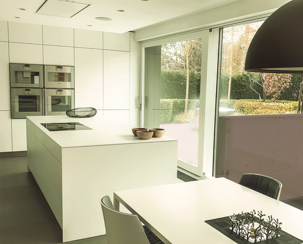 Photo of a large contemporary l-shaped open plan kitchen in Surrey with a drop-in sink, flat-panel cabinets, white cabinets, solid surface benchtops, white splashback, porcelain splashback, stainless steel appliances, porcelain floors, with island, grey floor, white benchtop and coffered.