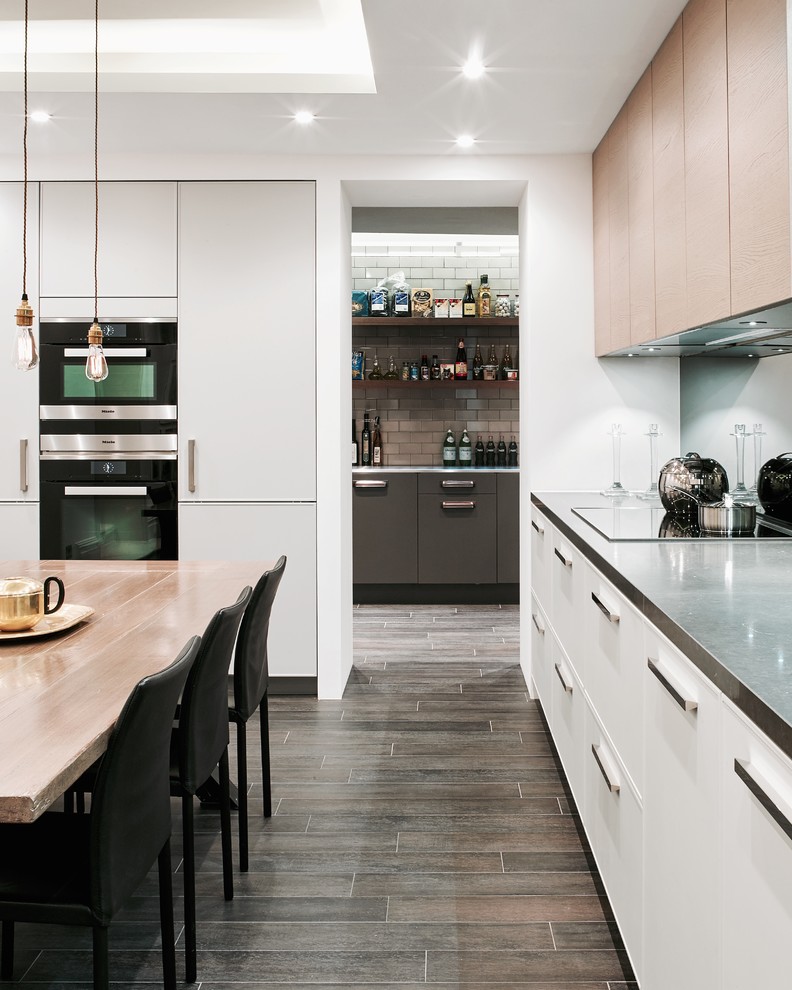 Design ideas for a contemporary eat-in kitchen in London with flat-panel cabinets, white cabinets, stainless steel appliances, granite benchtops, metallic splashback, mirror splashback, ceramic floors and brown floor.