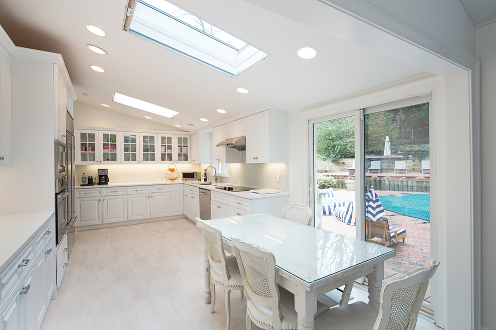 This is an example of a traditional u-shaped eat-in kitchen in New York with an undermount sink, raised-panel cabinets, white cabinets, white splashback, stainless steel appliances, light hardwood floors and no island.