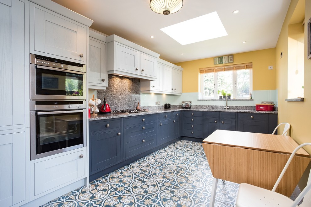 This is an example of a mid-sized transitional l-shaped eat-in kitchen in London with shaker cabinets, grey cabinets, granite benchtops, green splashback, glass sheet splashback, porcelain floors, no island and multi-coloured floor.