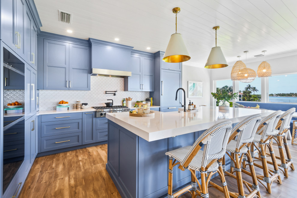 Mid-sized beach style l-shaped open plan kitchen in Other with a farmhouse sink, shaker cabinets, blue cabinets, quartz benchtops, white splashback, porcelain splashback, black appliances, porcelain floors, with island, brown floor, white benchtop and timber.
