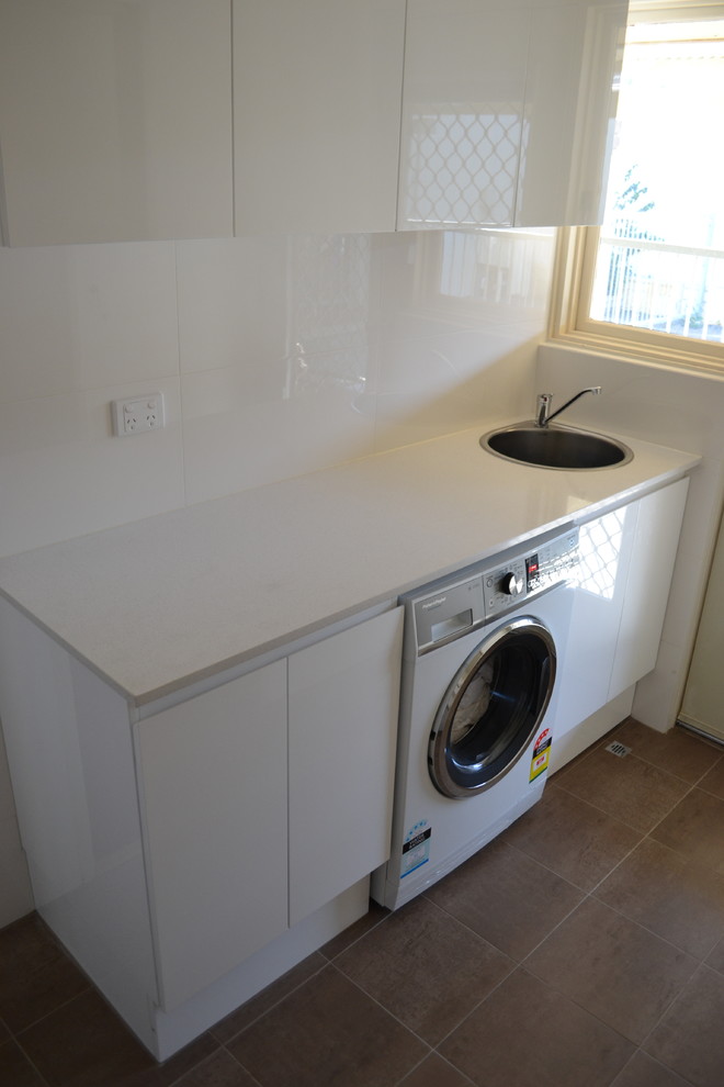 Photo of a small modern single-wall dedicated laundry room in Perth with a drop-in sink, louvered cabinets, white cabinets, quartz benchtops, white walls, porcelain floors, a side-by-side washer and dryer and white floor.