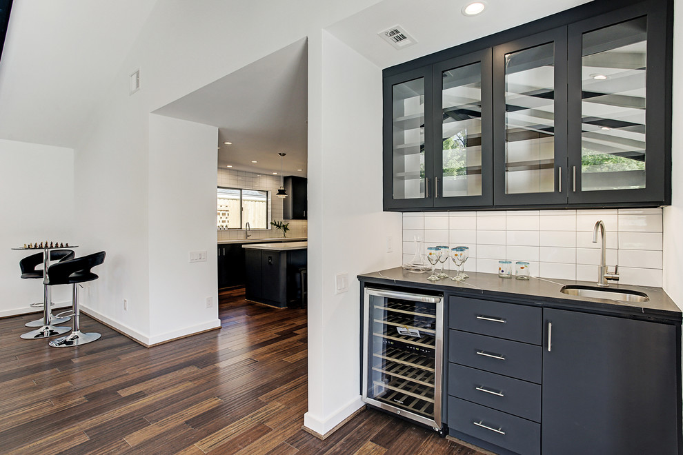 Inspiration for a midcentury single-wall wet bar in Houston with an undermount sink, flat-panel cabinets, black cabinets, quartz benchtops, white splashback, ceramic splashback, bamboo floors, brown floor and black benchtop.