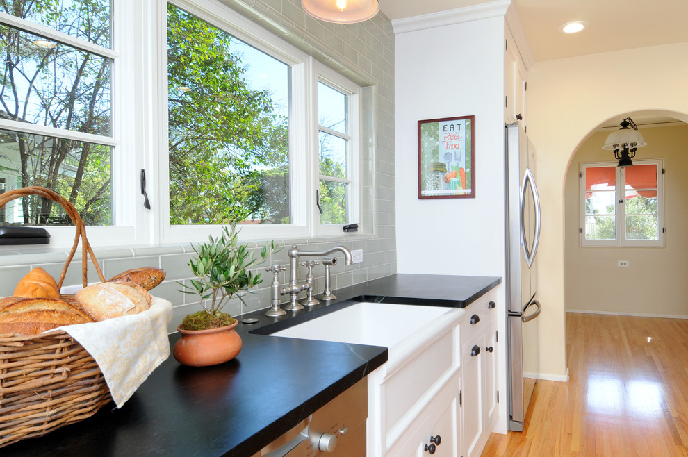 Photo of a traditional galley eat-in kitchen in Los Angeles with a farmhouse sink, shaker cabinets, white cabinets, soapstone benchtops, green splashback, subway tile splashback and stainless steel appliances.