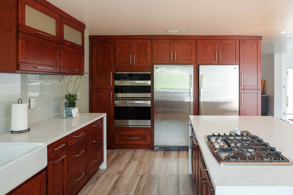 This is an example of an expansive contemporary u-shaped eat-in kitchen in Orange County with a single-bowl sink, shaker cabinets, white cabinets, quartz benchtops, white splashback, glass tile splashback, stainless steel appliances, light hardwood floors, with island, beige floor and white benchtop.