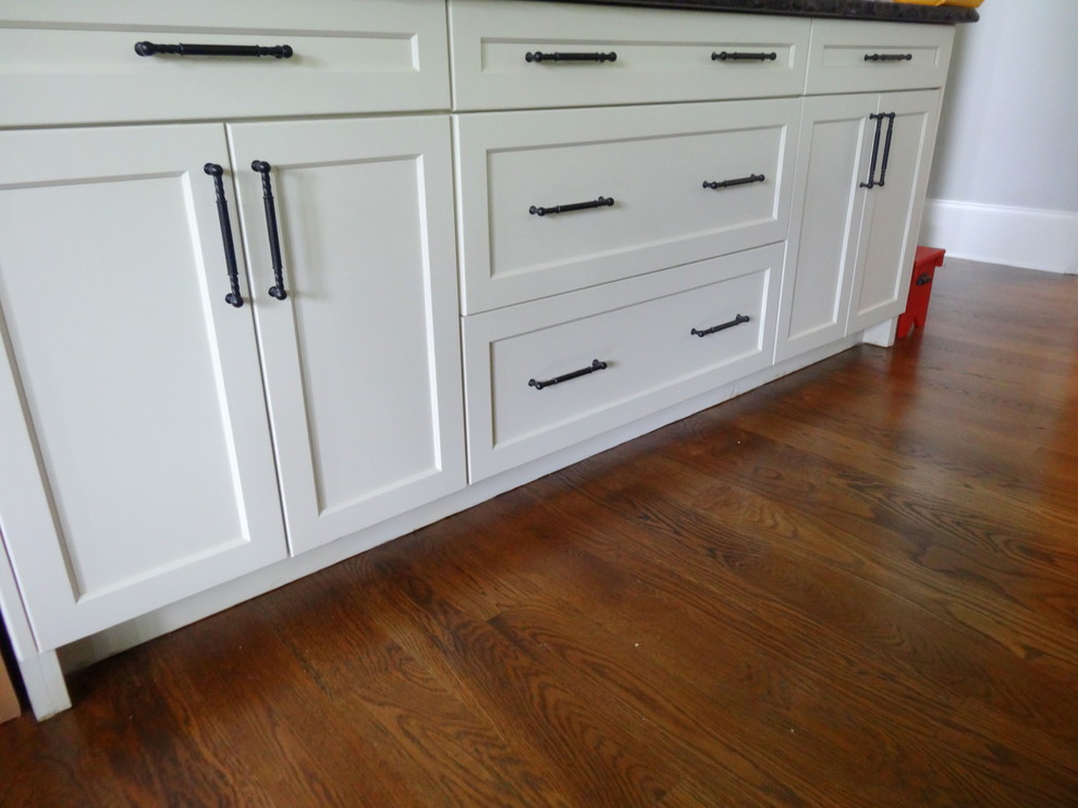 Inspiration for a mid-sized transitional l-shaped medium tone wood floor open concept kitchen remodel in Charlotte with a farmhouse sink, shaker cabinets, white cabinets, granite countertops, beige backsplash, subway tile backsplash, stainless steel appliances and an island