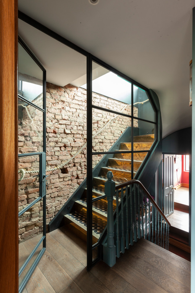 ロンドンにある高級な広いコンテンポラリースタイルのおしゃれな折り返し階段 (金属の蹴込み板、ワイヤーの手すり、レンガ壁) の写真