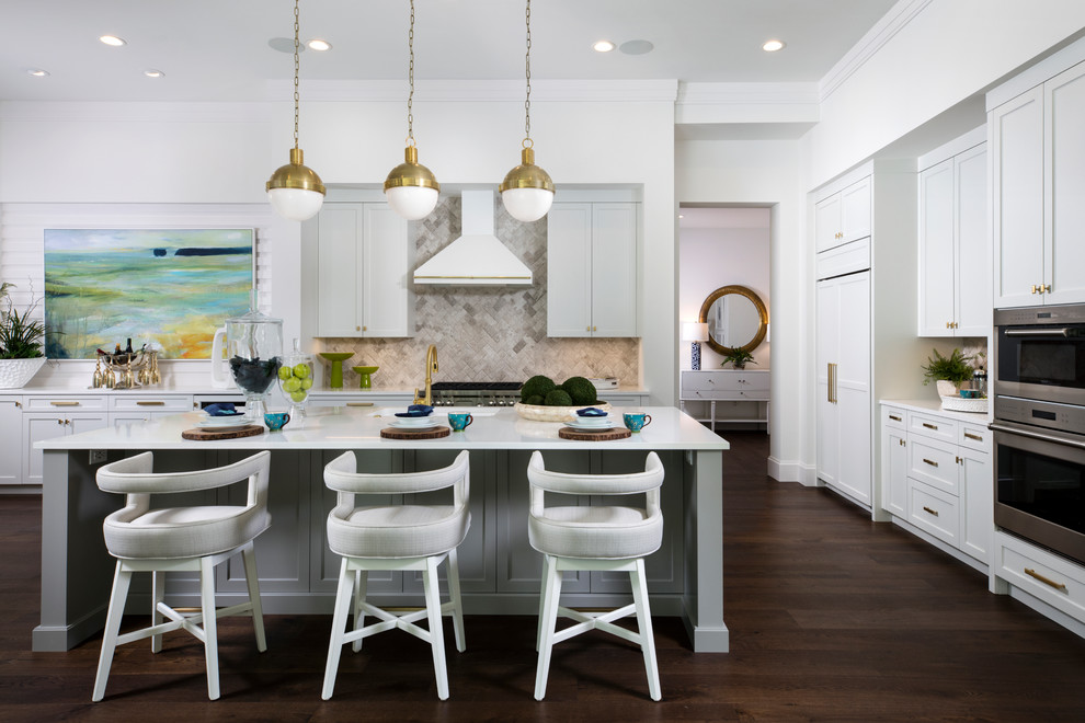 This is an example of a transitional l-shaped kitchen in Tampa with shaker cabinets, white cabinets, grey splashback, stainless steel appliances, dark hardwood floors, with island, brown floor and white benchtop.