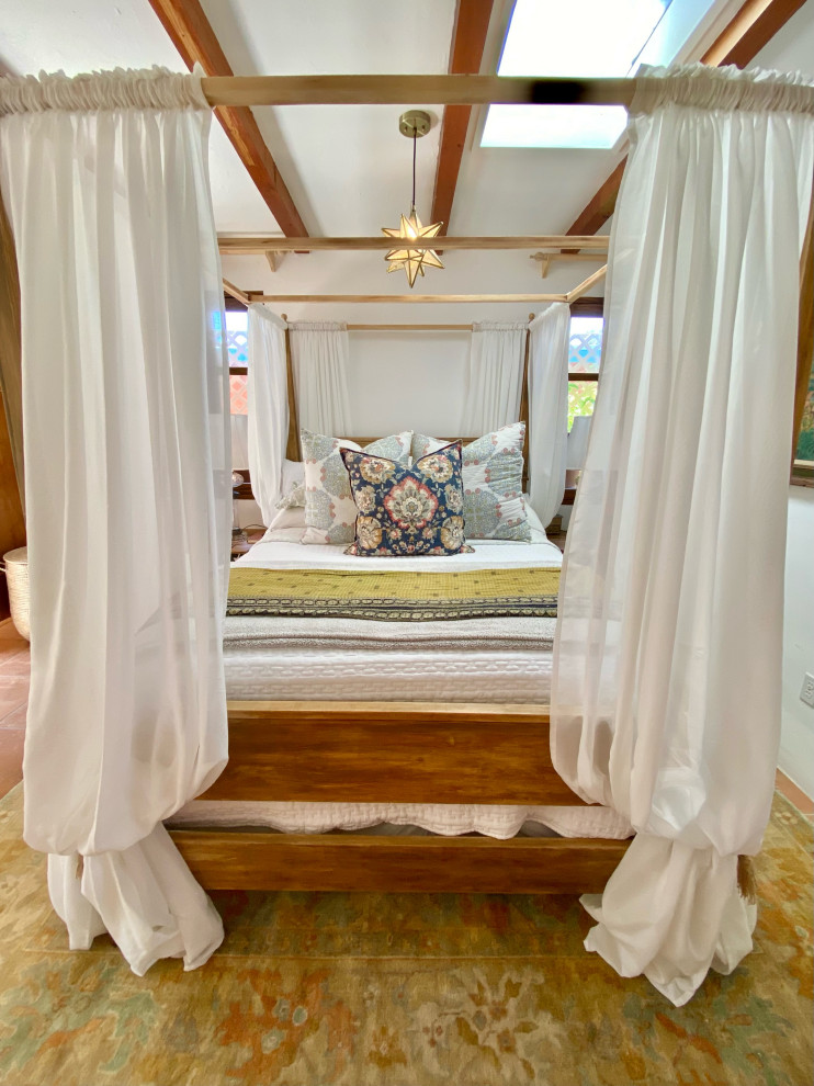 На фото: гостевая спальня среднего размера, (комната для гостей) в морском стиле с белыми стенами, полом из терракотовой плитки, угловым камином, фасадом камина из штукатурки, оранжевым полом, балками на потолке и кирпичными стенами с