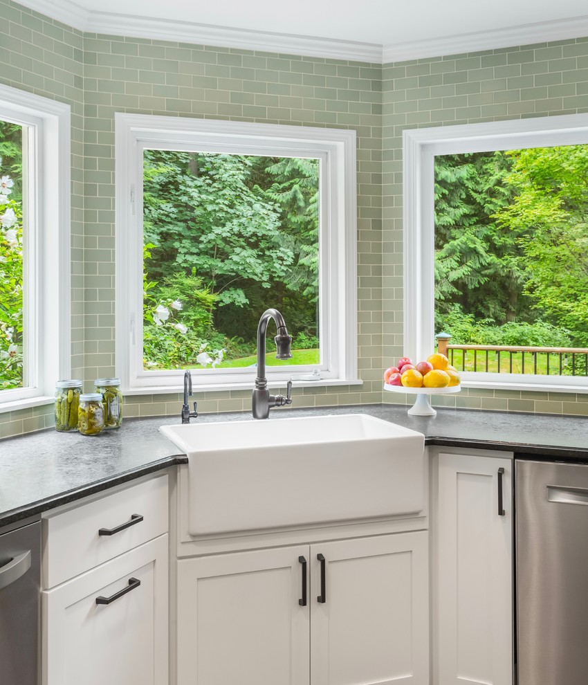 This is an example of a mid-sized country u-shaped open plan kitchen in Seattle with a farmhouse sink, shaker cabinets, white cabinets, soapstone benchtops, green splashback, ceramic splashback, stainless steel appliances, medium hardwood floors, with island and brown floor.