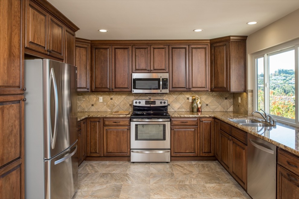 This is an example of a traditional u-shaped eat-in kitchen in San Diego with a drop-in sink, raised-panel cabinets, brown cabinets, granite benchtops, beige splashback, stone tile splashback and stainless steel appliances.