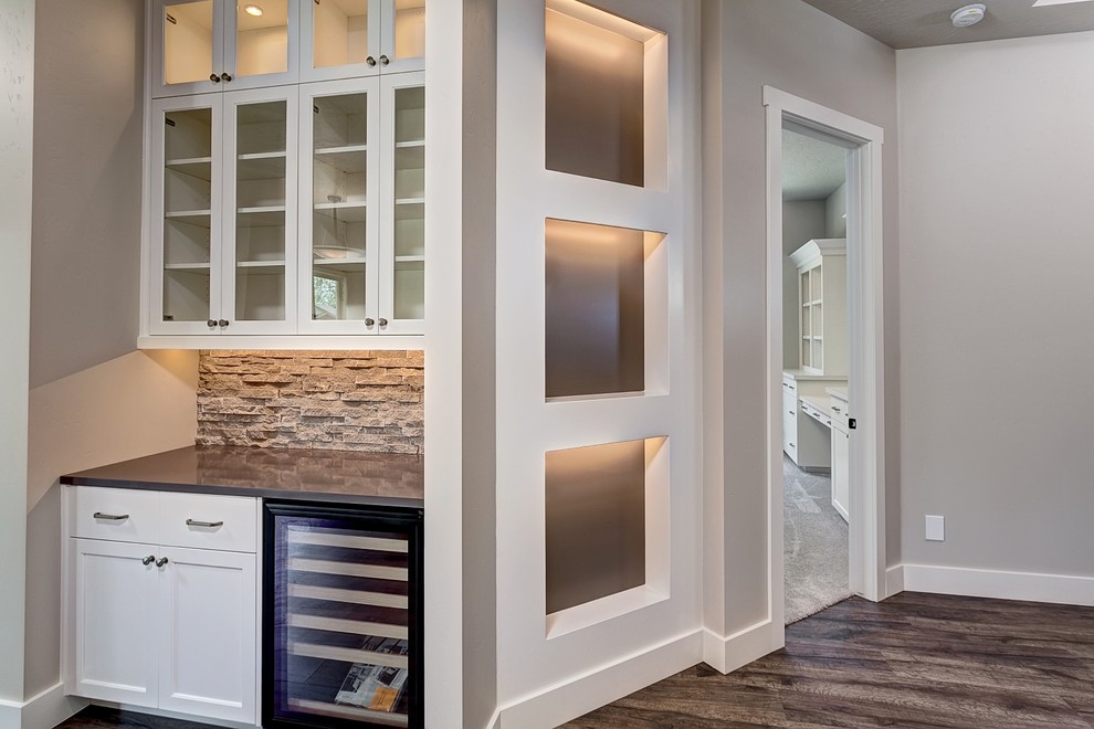Design ideas for a mid-sized arts and crafts single-wall wet bar in Boise with no sink, glass-front cabinets, white cabinets, quartz benchtops, grey splashback, stone tile splashback and dark hardwood floors.