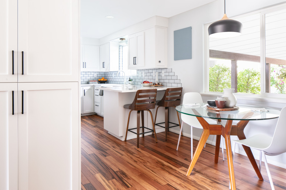 Inspiration for a mid-sized transitional u-shaped eat-in kitchen in Boise with a farmhouse sink, white cabinets, blue splashback, ceramic splashback, medium hardwood floors, no island, brown floor and white benchtop.