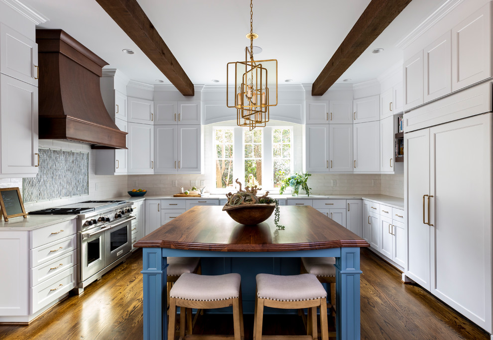Design ideas for a traditional u-shaped kitchen in Charlotte with shaker cabinets, white cabinets, white splashback, subway tile splashback, panelled appliances, dark hardwood floors, with island, brown floor and white benchtop.