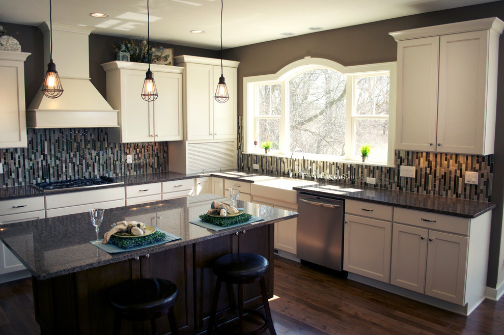 Photo of a mid-sized transitional u-shaped kitchen in Milwaukee with a farmhouse sink, recessed-panel cabinets, white cabinets, granite benchtops, multi-coloured splashback, matchstick tile splashback, stainless steel appliances, dark hardwood floors and with island.
