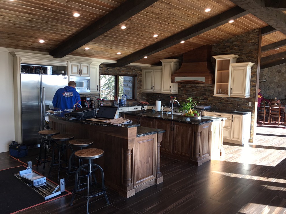 Inspiration for a huge rustic l-shaped porcelain tile open concept kitchen remodel with a drop-in sink, dark wood cabinets, granite countertops, beige backsplash, stone tile backsplash, stainless steel appliances and two islands