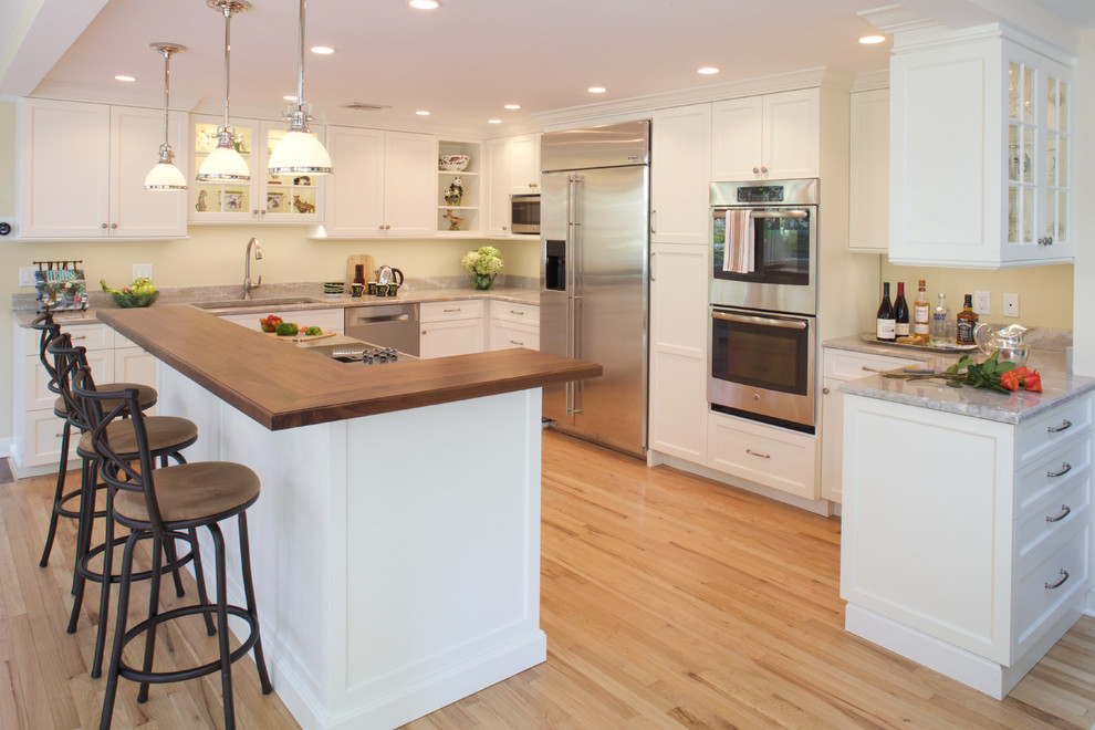 Example of a mid-sized transitional l-shaped light wood floor eat-in kitchen design in New York with recessed-panel cabinets, stainless steel appliances, an island, an undermount sink, white cabinets and quartzite countertops