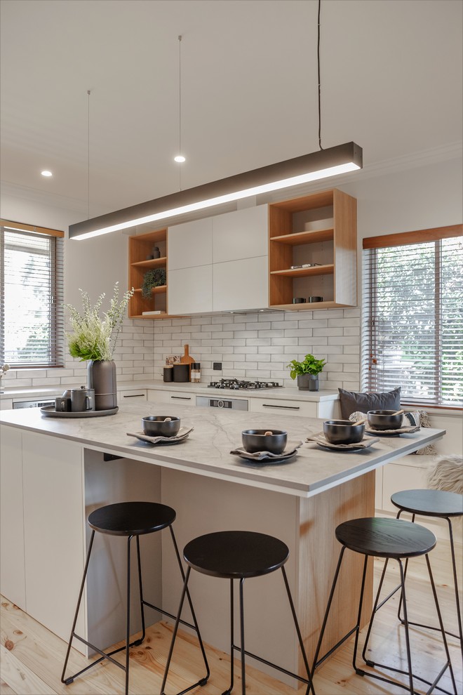 Design ideas for a large contemporary u-shaped eat-in kitchen in Adelaide with a double-bowl sink, flat-panel cabinets, white cabinets, quartz benchtops, white splashback, subway tile splashback, black appliances, light hardwood floors, with island, yellow floor and grey benchtop.