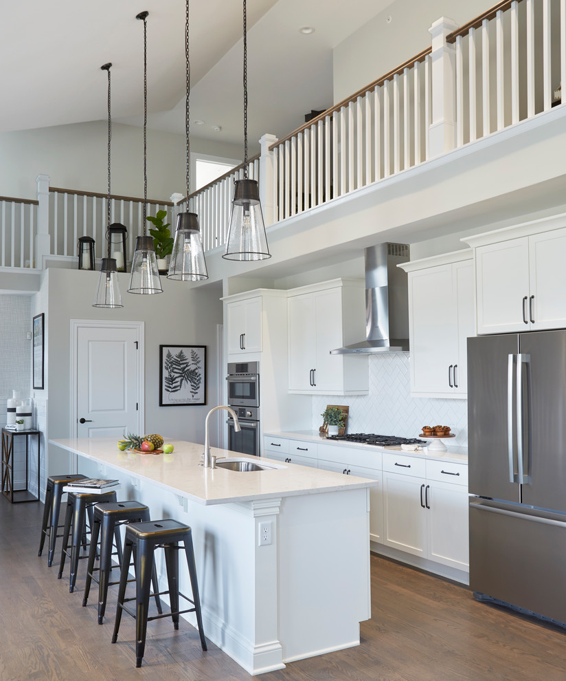 Inspiration for a beach style single-wall kitchen in Chicago with white cabinets, quartz benchtops, white splashback, stainless steel appliances, medium hardwood floors, with island, white benchtop, an undermount sink and shaker cabinets.