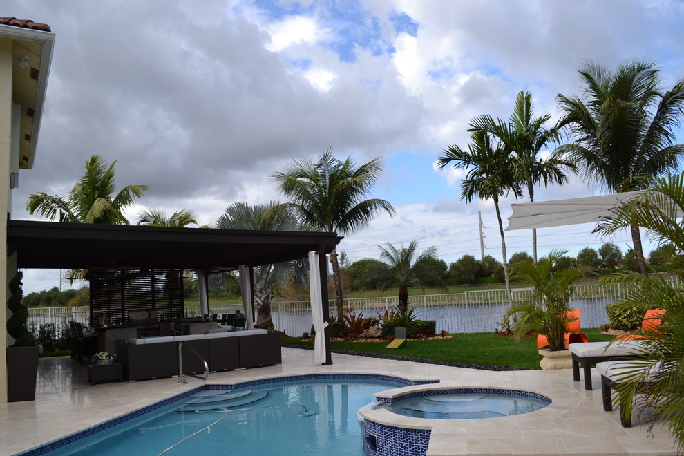 Expansive tropical backyard patio in Miami with an outdoor kitchen, natural stone pavers and a pergola.