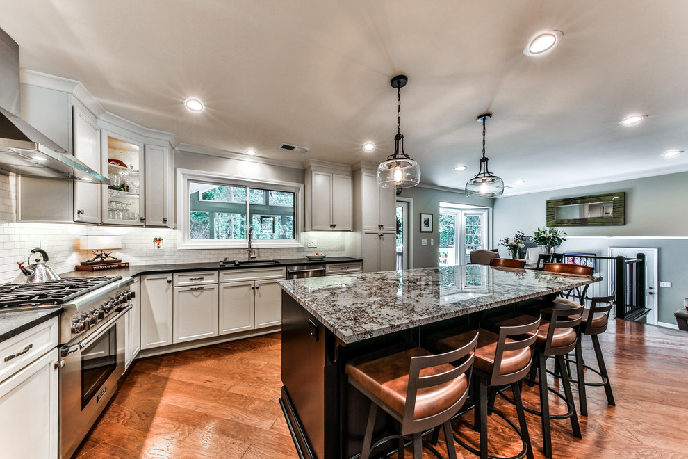 Open concept kitchen - large transitional l-shaped medium tone wood floor open concept kitchen idea in Atlanta with an undermount sink, shaker cabinets, white cabinets, granite countertops, white backsplash, subway tile backsplash, stainless steel appliances and an island