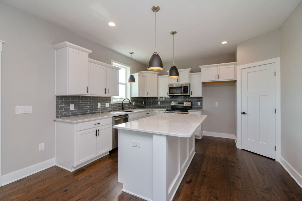 Mid-sized transitional dark wood floor and brown floor kitchen photo with an undermount sink, shaker cabinets, white cabinets, quartz countertops, gray backsplash, subway tile backsplash, stainless steel appliances, an island and white countertops
