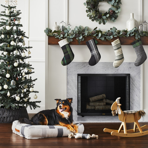 Holiday Decor Ideas for Dog Lovers - Black and white dog lying on black and white bed in front of fireplace.  Christmas tree in background