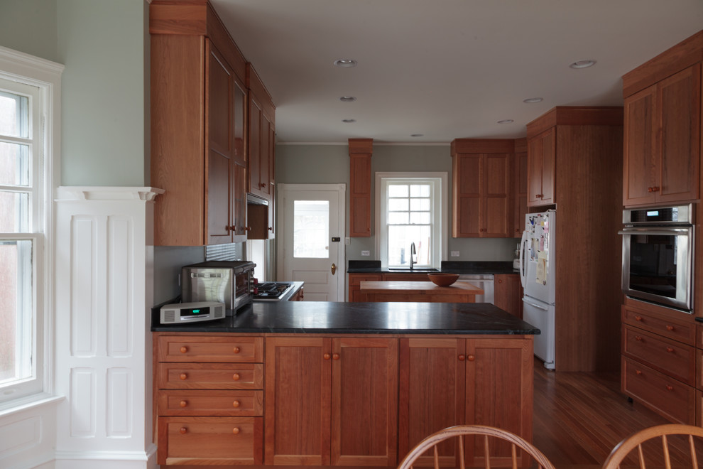 Inspiration for a mid-sized arts and crafts u-shaped eat-in kitchen in Philadelphia with an undermount sink, recessed-panel cabinets, brown cabinets, soapstone benchtops, stainless steel appliances, light hardwood floors, a peninsula and brown floor.