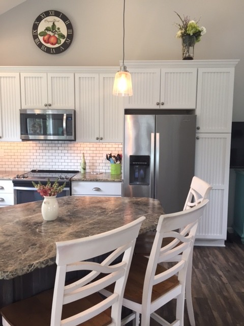 Design ideas for a mid-sized beach style l-shaped eat-in kitchen in Baltimore with an undermount sink, flat-panel cabinets, white cabinets, laminate benchtops, white splashback, subway tile splashback, stainless steel appliances, dark hardwood floors, with island and brown floor.