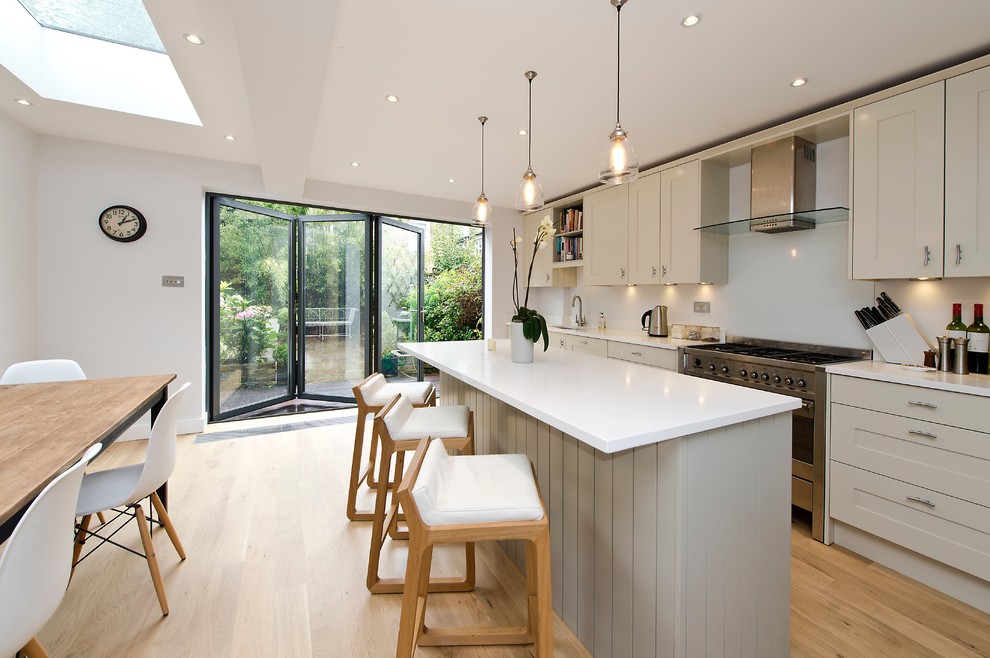 Photo of a mid-sized contemporary single-wall eat-in kitchen in London with an undermount sink, recessed-panel cabinets, grey cabinets, quartzite benchtops, glass sheet splashback, stainless steel appliances, light hardwood floors, with island, beige floor and white benchtop.