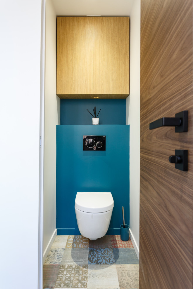 Inspiration for a small contemporary powder room in Paris with light wood cabinets, a wall-mount toilet, blue walls, laminate floors, multi-coloured floor and a built-in vanity.