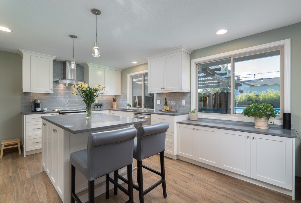 Photo of a mid-sized transitional l-shaped open plan kitchen in Portland with an undermount sink, shaker cabinets, white cabinets, quartz benchtops, grey splashback, ceramic splashback, stainless steel appliances, porcelain floors, with island and brown floor.