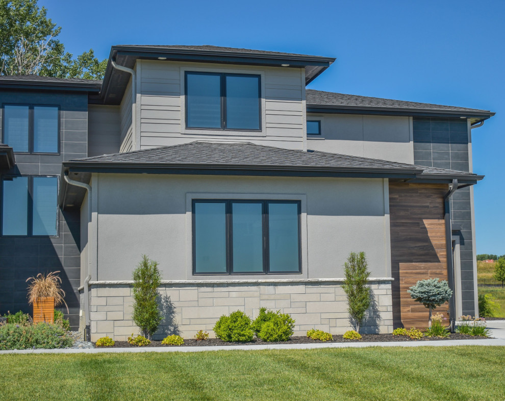 This is an example of a modern black house exterior in Omaha with stone veneer, a shingle roof and a black roof.