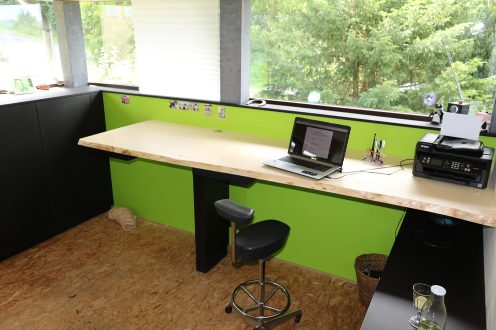 Mittelgroßes Modernes Arbeitszimmer ohne Kamin mit grüner Wandfarbe, Sperrholzboden, Einbau-Schreibtisch, Arbeitsplatz und braunem Boden
