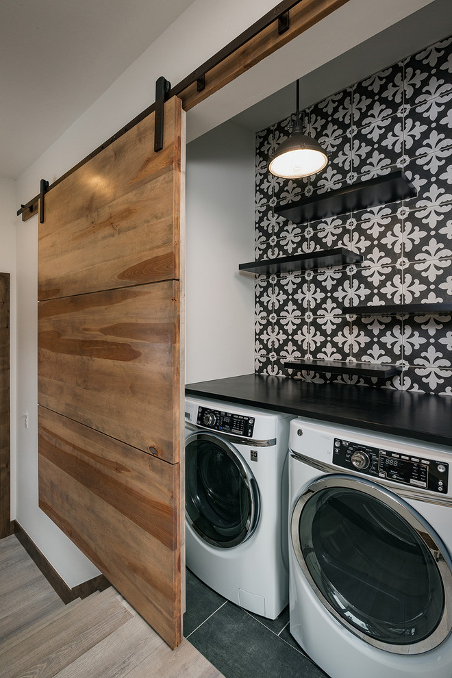 Inspiration for a small contemporary single-wall laundry cupboard in Denver with open cabinets, black cabinets, quartz benchtops, multi-coloured walls, ceramic floors, a side-by-side washer and dryer, black floor and black benchtop.