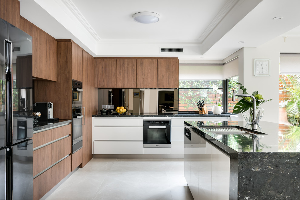 This is an example of a large contemporary l-shaped kitchen in Perth with an undermount sink, flat-panel cabinets, medium wood cabinets, black splashback, black appliances, with island, beige floor and black benchtop.