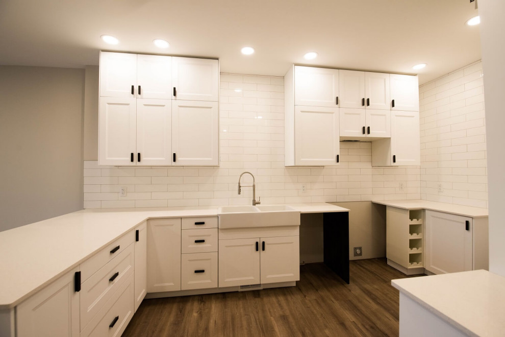 Mid-sized contemporary single-wall eat-in kitchen in Other with a farmhouse sink, shaker cabinets, white cabinets, quartzite benchtops, white splashback, ceramic splashback, vinyl floors, a peninsula, brown floor and white benchtop.