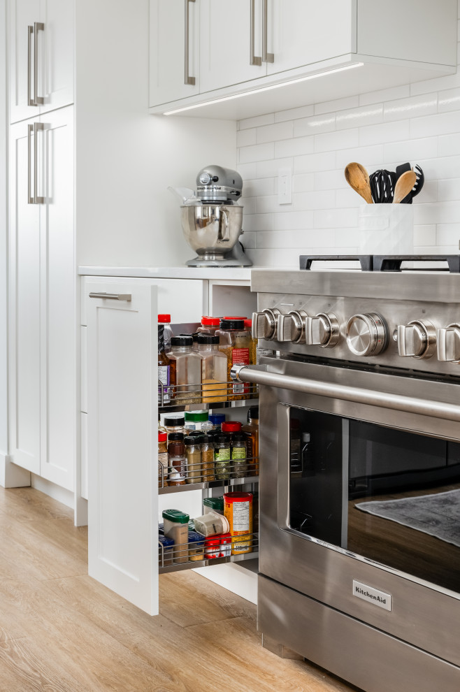 Inspiration for a mid-sized transitional l-shaped light wood floor and beige floor eat-in kitchen remodel in Vancouver with an undermount sink, shaker cabinets, white cabinets, quartzite countertops, white backsplash, subway tile backsplash, stainless steel appliances, an island and white countertops