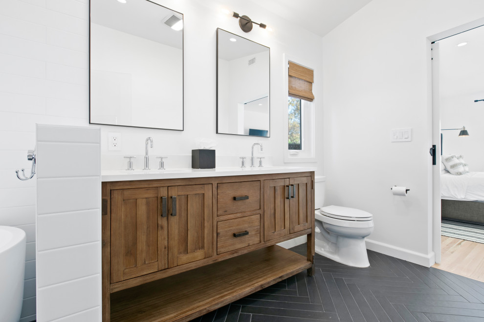 This is an example of a large transitional master wet room bathroom in Los Angeles with furniture-like cabinets, brown cabinets, a freestanding tub, white tile, subway tile, porcelain floors, engineered quartz benchtops, black floor, a hinged shower door and white benchtops.