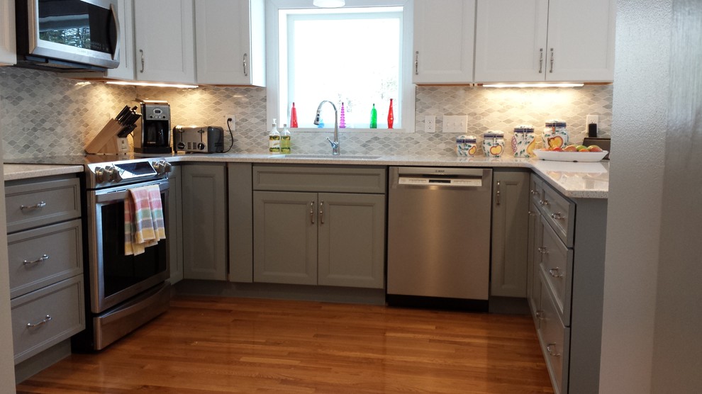 Inspiration for a mid-sized transitional u-shaped light wood floor kitchen remodel in Boston with a single-bowl sink, gray cabinets, quartz countertops, gray backsplash, mosaic tile backsplash, stainless steel appliances and a peninsula