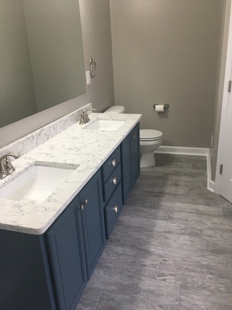 Inspiration for a mid-sized contemporary master bathroom in Raleigh with beaded inset cabinets, blue cabinets, a hot tub, an alcove shower, a one-piece toilet, gray tile, porcelain tile, grey walls, ceramic floors, an undermount sink, quartzite benchtops, multi-coloured floor, a sliding shower screen and white benchtops.