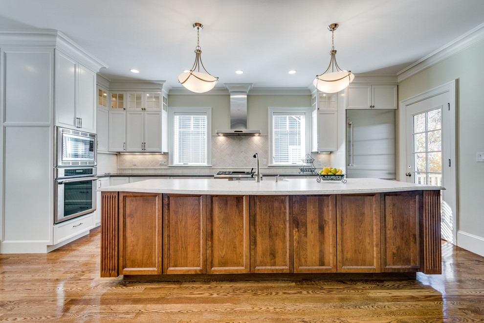 Open concept kitchen - mid-sized transitional l-shaped medium tone wood floor and brown floor open concept kitchen idea in Boston with a farmhouse sink, recessed-panel cabinets, white cabinets, soapstone countertops, beige backsplash, ceramic backsplash, stainless steel appliances and an island