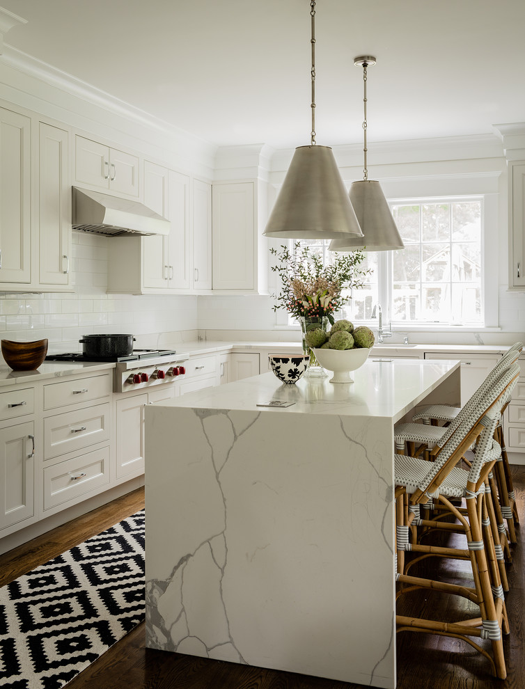 Photo of a transitional l-shaped kitchen in Boston with shaker cabinets, white cabinets, white splashback, subway tile splashback, stainless steel appliances, dark hardwood floors, with island and white benchtop.