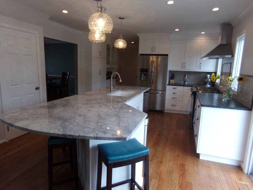 Mid-sized transitional l-shaped medium tone wood floor eat-in kitchen photo in New York with an undermount sink, recessed-panel cabinets, white cabinets, granite countertops, gray backsplash, ceramic backsplash, stainless steel appliances and an island